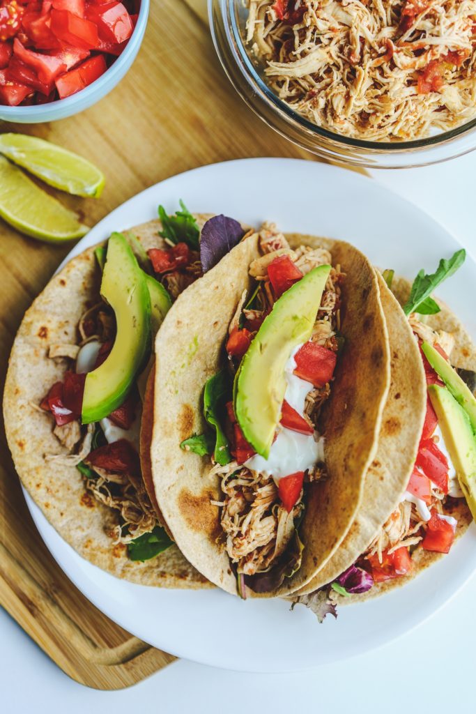 tacos on plate with bowl of shredded chicken and limes