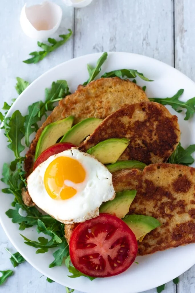 three slices of French toast topped with avocado tomatoes and fried egg