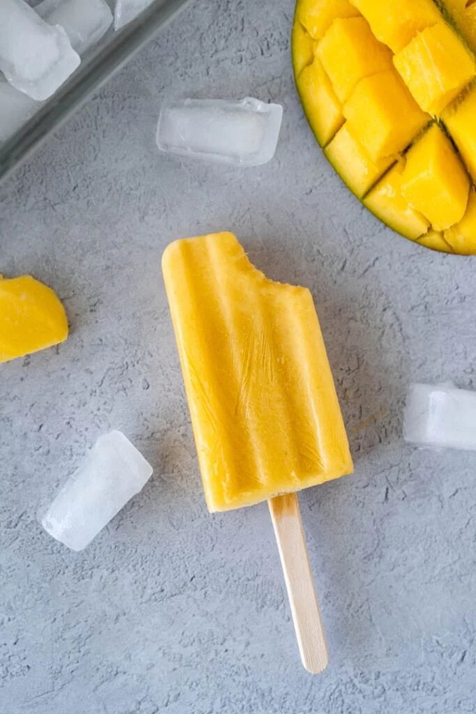 mango popsicle with bite taken out surrounded by ice cubes