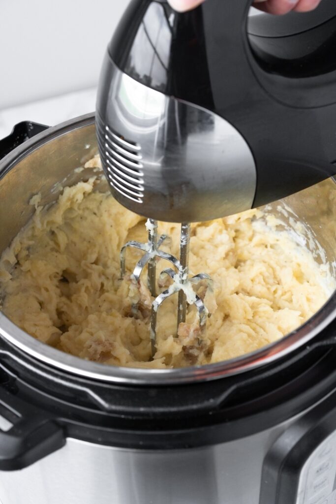 Instant Pot filled with mashed potatoes being stirred by a hand mixer