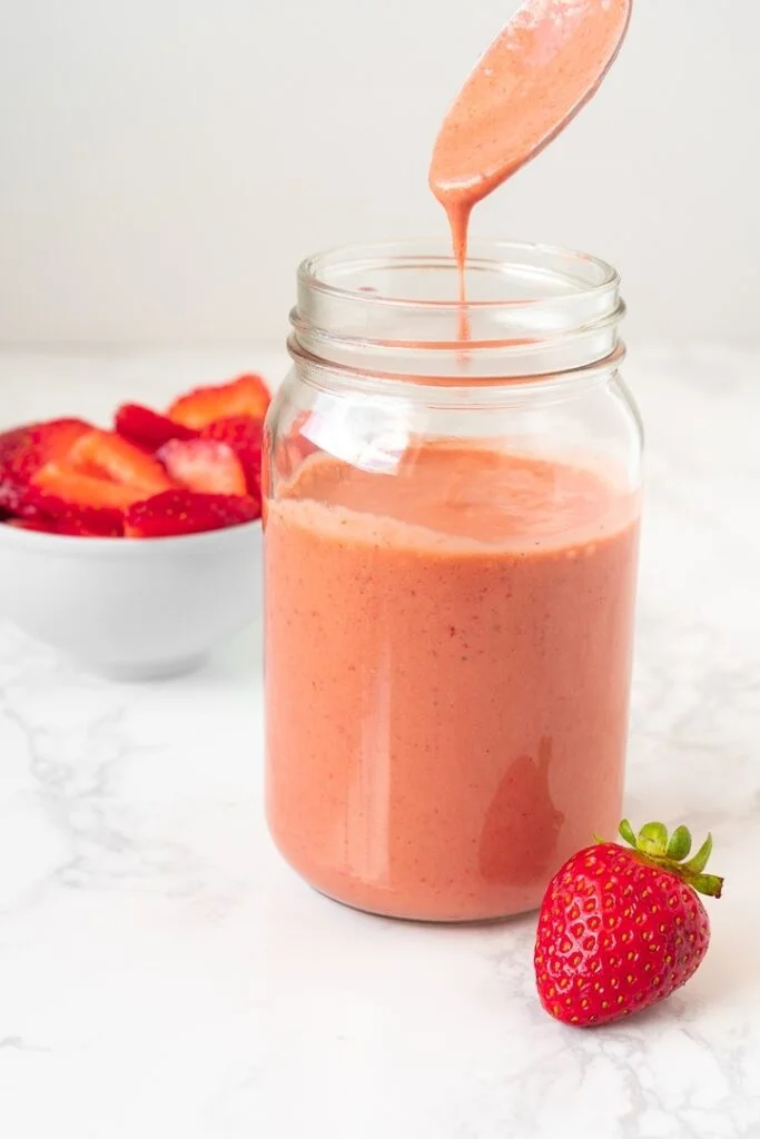 jar with pink dressing next to sliced strawberry and whole strawberry