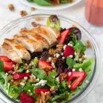 plate and bowl containing strawberry walnut salad with chicken