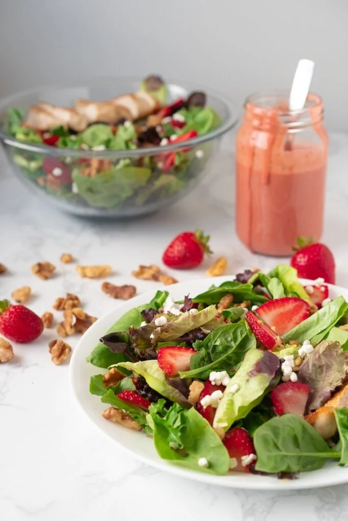 plate and bowl containing strawberry walnut salad and strawberry dressing