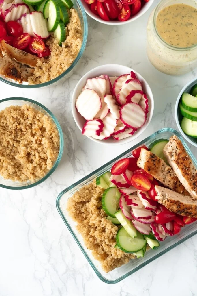 rectangular food container with quinoa, chicken and vegetables and circular prep bowls with ingredients