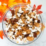 clear bowl with popcorn, pecans, dried apples, and cereal against a white background with fall leaves