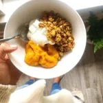 hand holding bowl with yogurt, pumpkin puree, and granola