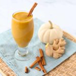 glass with pumpkin smoothie and pumpkin, cinnamon, and ginger root in background