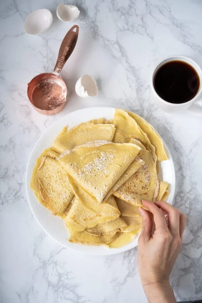 hand reaching for plate of crepes