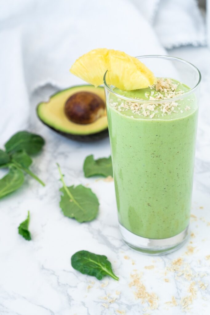 green smoothie garnished with pineapple wedge and shredded coconut