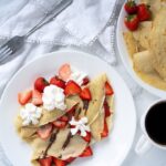plate of crepes topped with strawberries, Nutella, and whipped cream