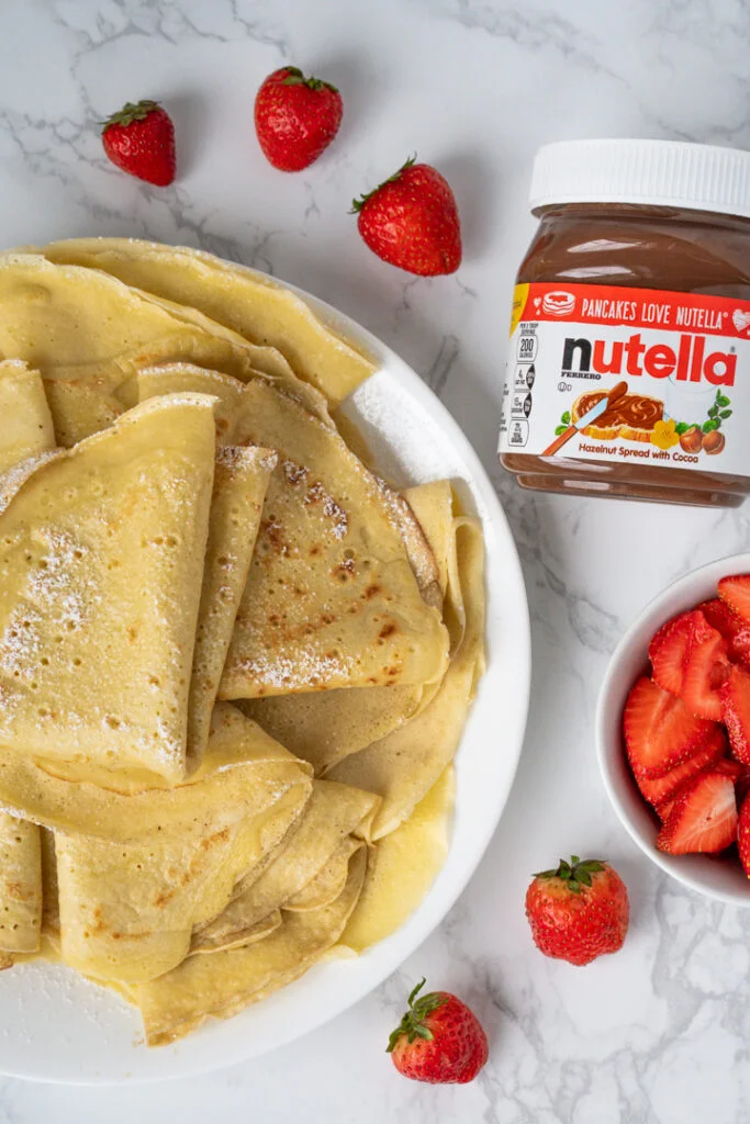 plate of plain crepes with jar of Nutella and bowl of strawberries