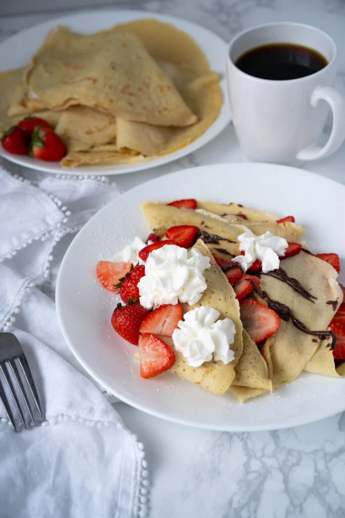 plate of crepes topped with strawberries, whipped cream, and Nutella