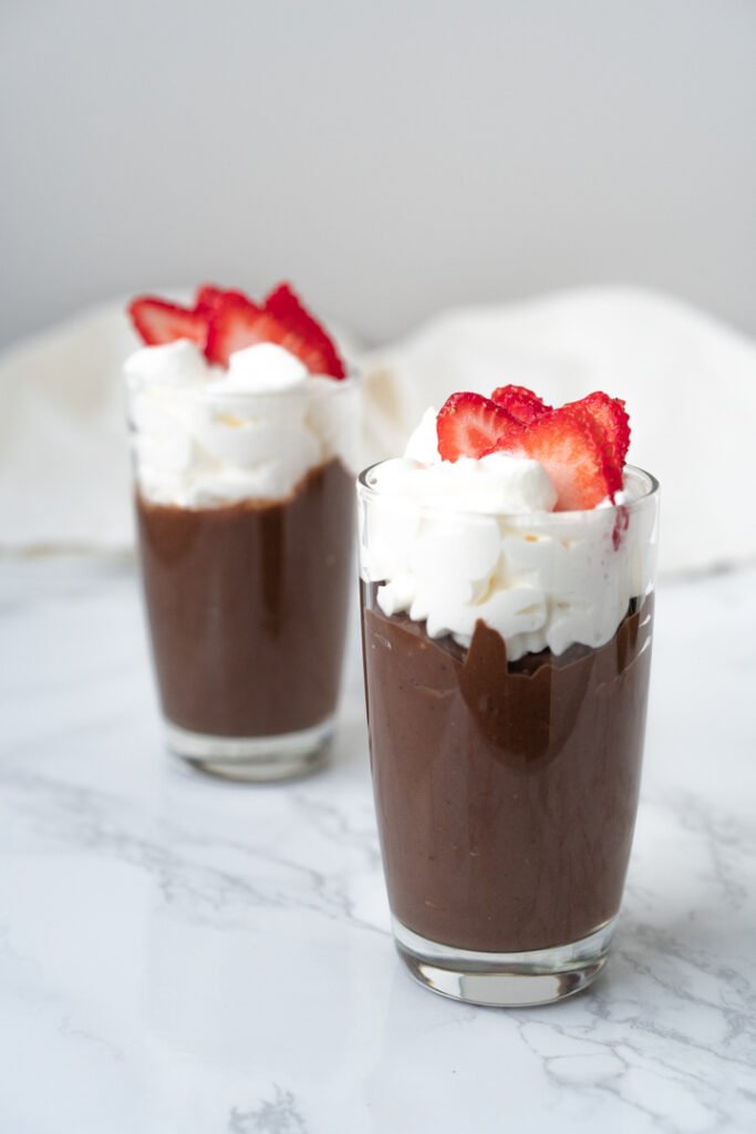 two cups of chocolate mousse topped with strawberries and whipped cream
