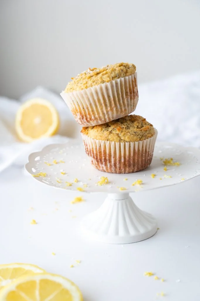 two lemon poppyseed muffins stacked on white cake plate