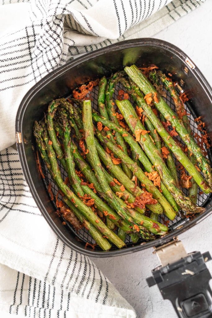 air fryer basket filled with cooked asparagus and parmesan cheese