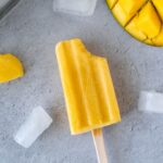 mango popsicle with bite taken out surrounded by ice cubes