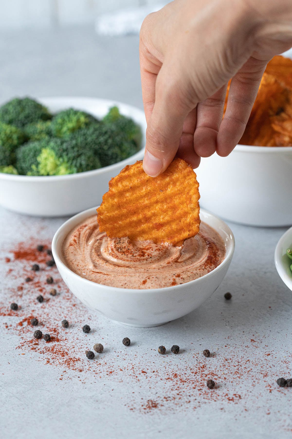 hand dipping barbecue chip in small cup of creamy dip