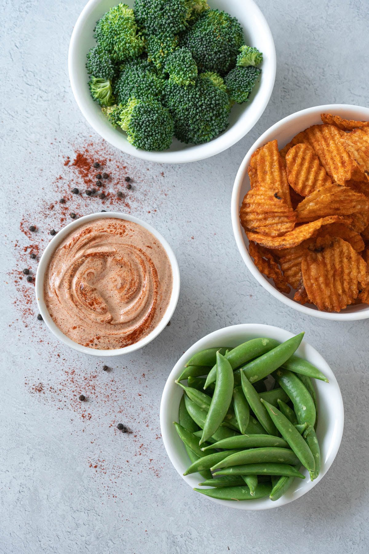 white bowls filled with aioli dip, broccoli, barbecue chips, and snap peas