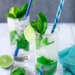 two highball glasses filled with crushed ice, water, and mint, topped with colorful straws, lime, and mint