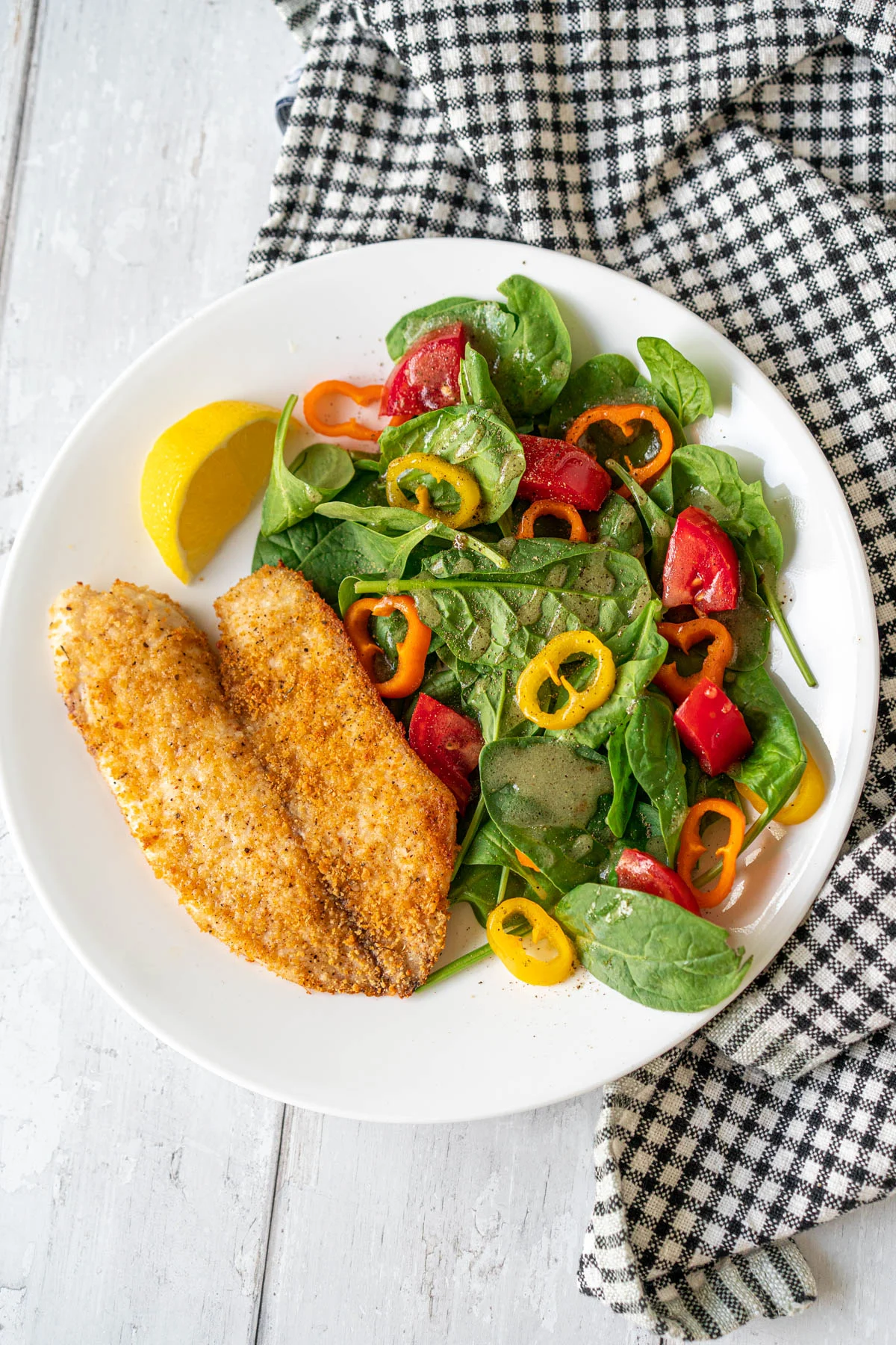 tilapia filet and salad on a white plate with a checkered napkin in the background 