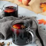 two clear mugs of mulled wine with sliced fruit and spices