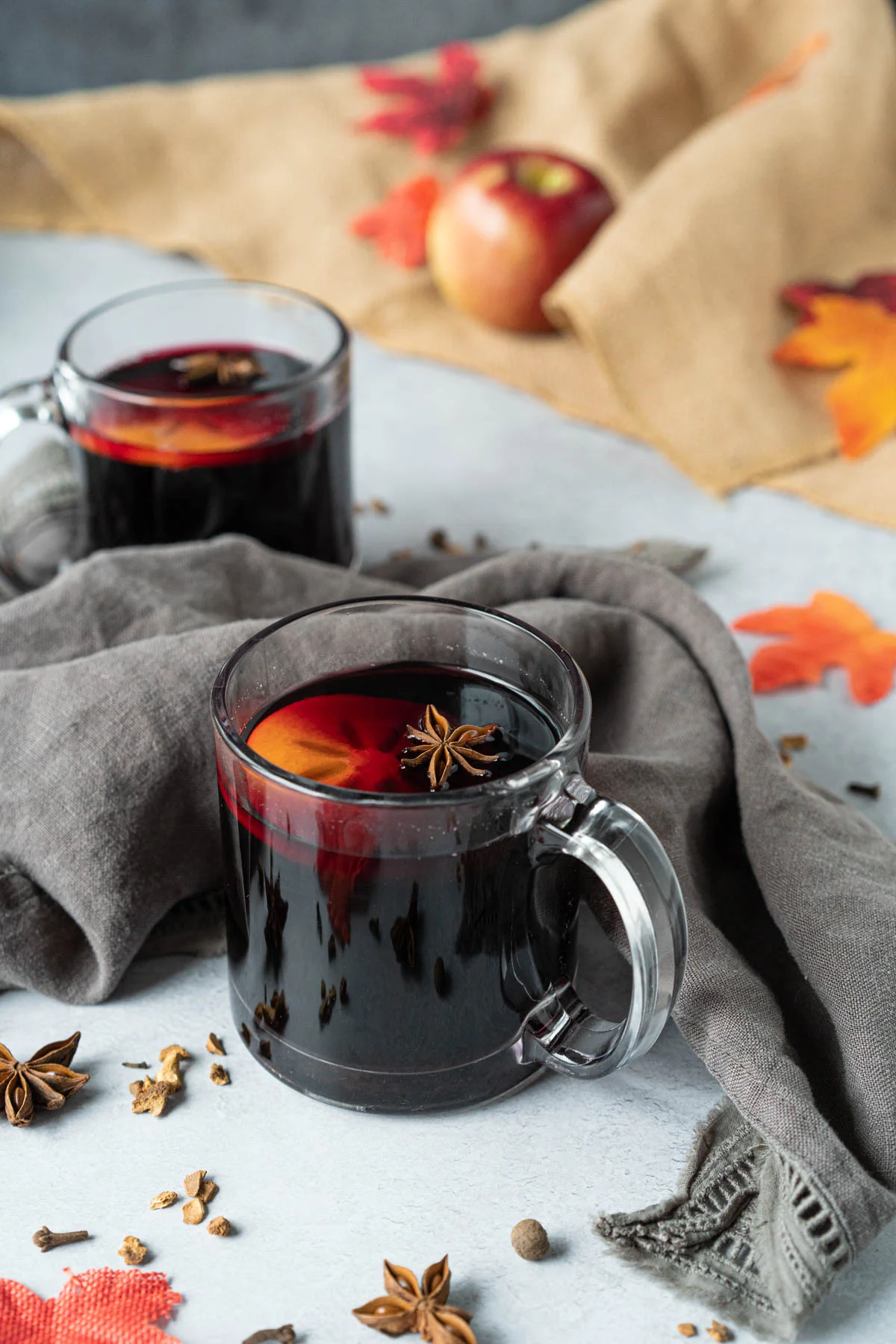 two clear mugs of mulled wine with a persimmon slice and star anise pod