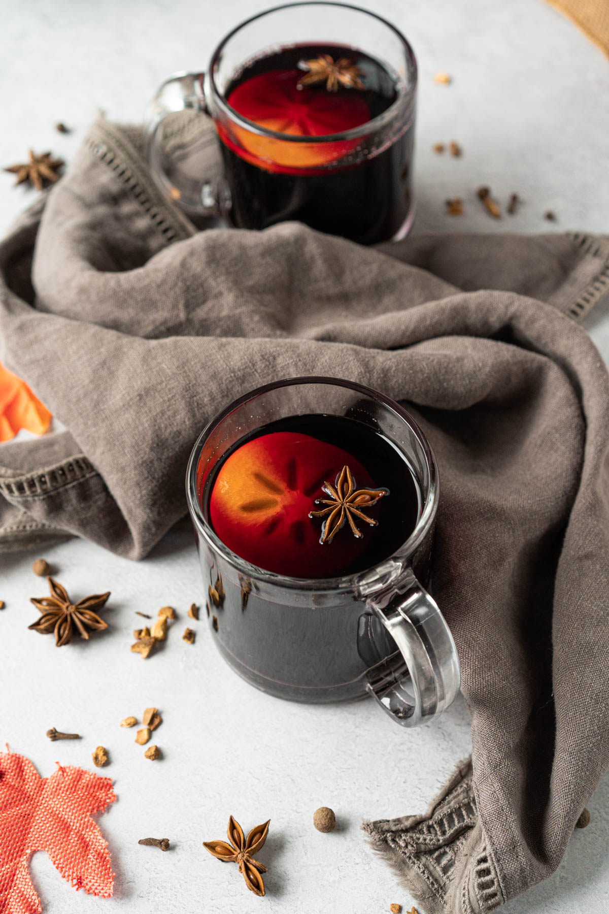 two mugs of mulled wine with a sliced persimmon and star anise pod