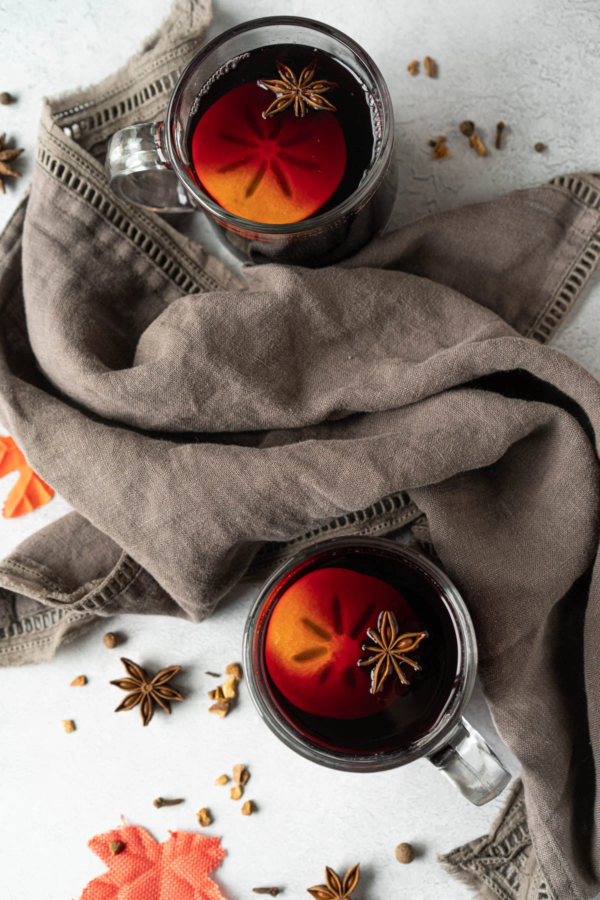 two mugs of mulled wine with a persimmon slice and a star anise pod