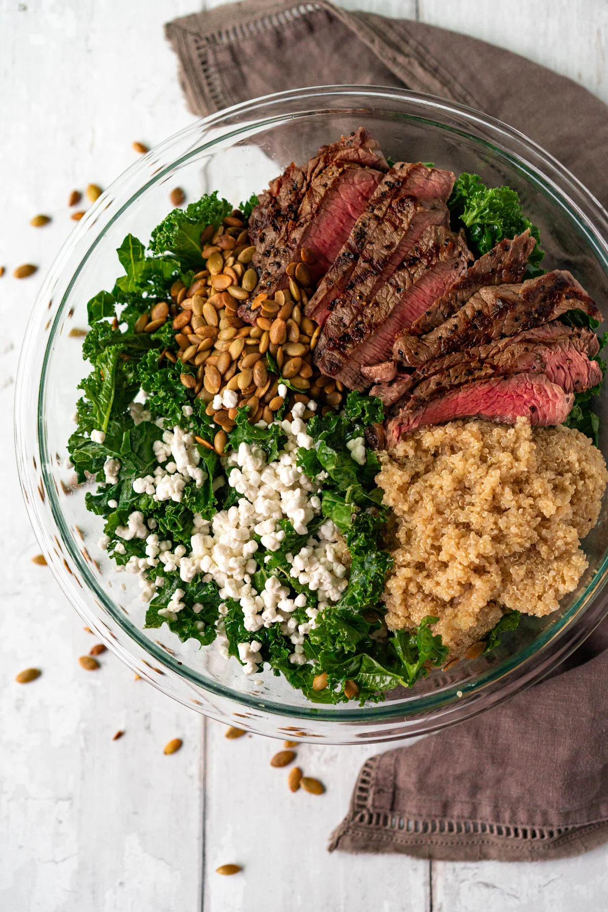 large bowl with kale, goat cheese, pipits, sliced steak, and quinoa