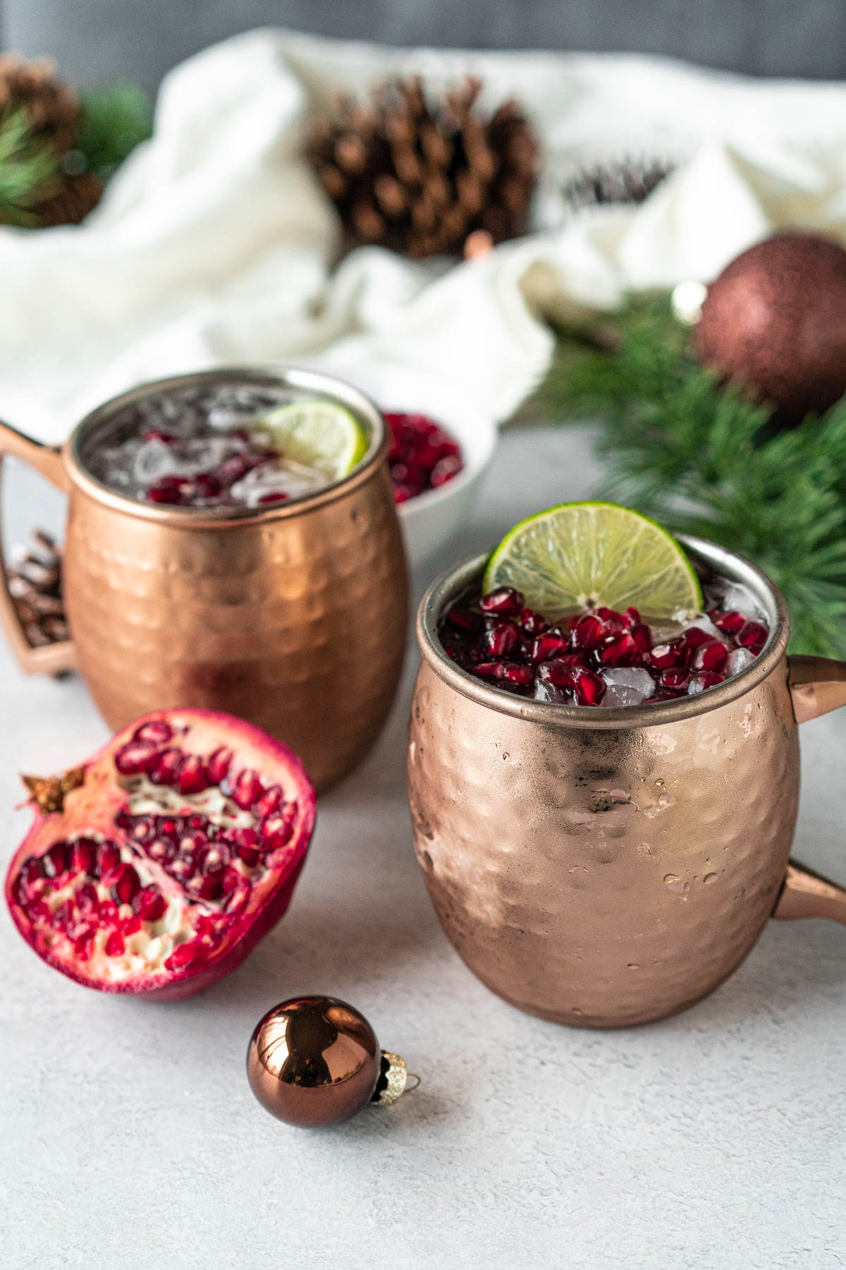 two copper mugs filled with ice and topped with pomegranate arils and a lime slice