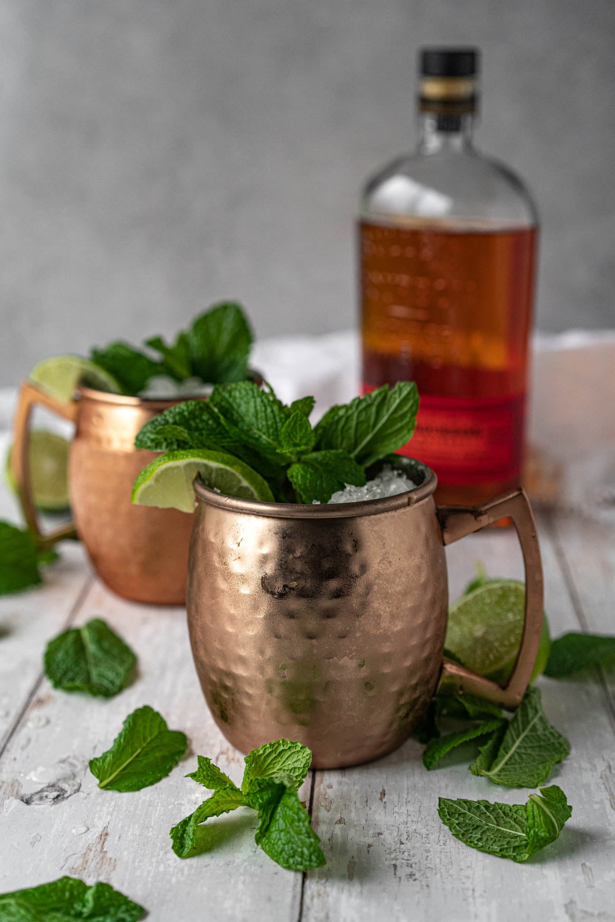 two frosted mugs garnished with lime and mint with bottle of whiskey in the background