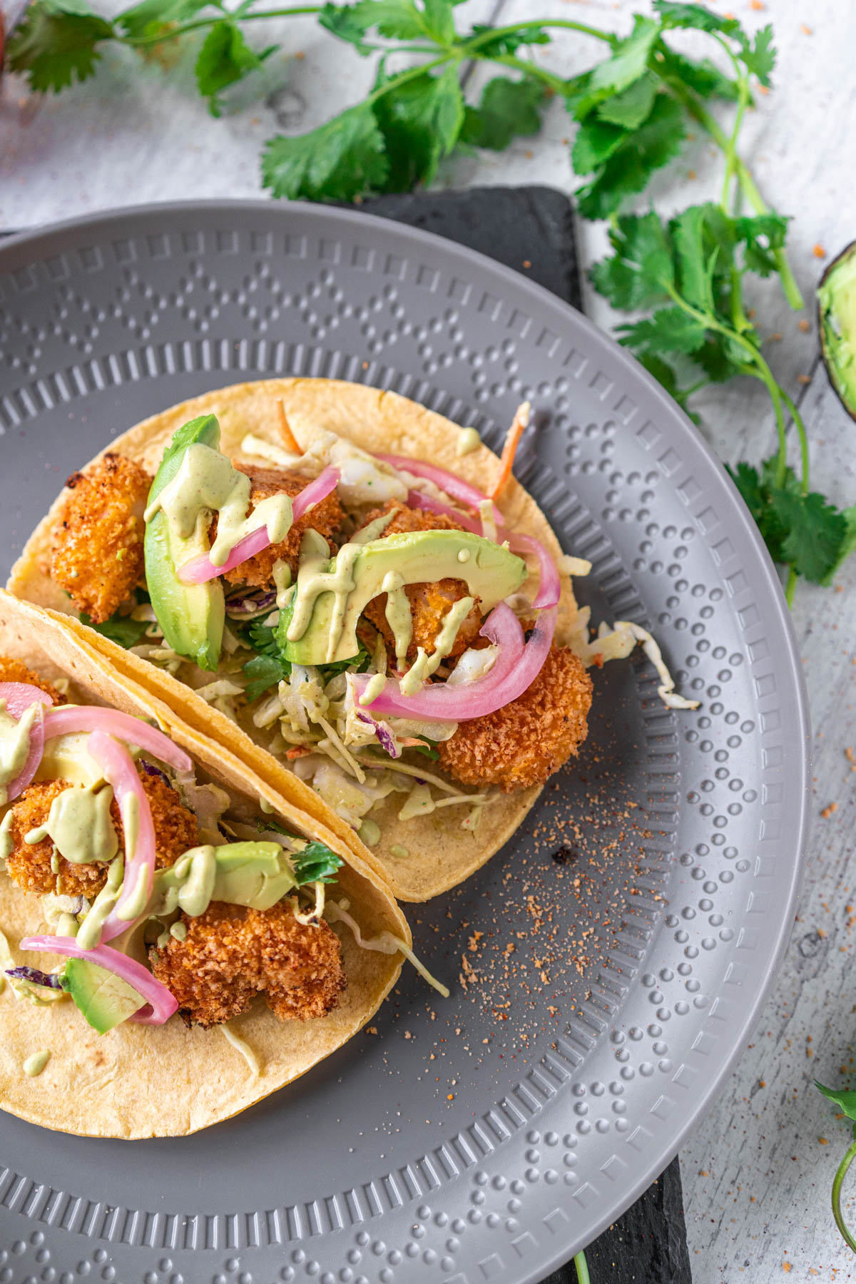 grey plate with two tacos filled with breaded seafood, avocado, and pickled onions