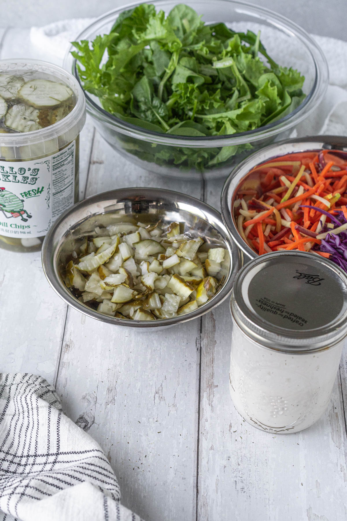 ingredients for a pickle salad (pickles, lettuce, shredded carrots, shredded cabbage, ranch dressing) arranged in bowls and jars
