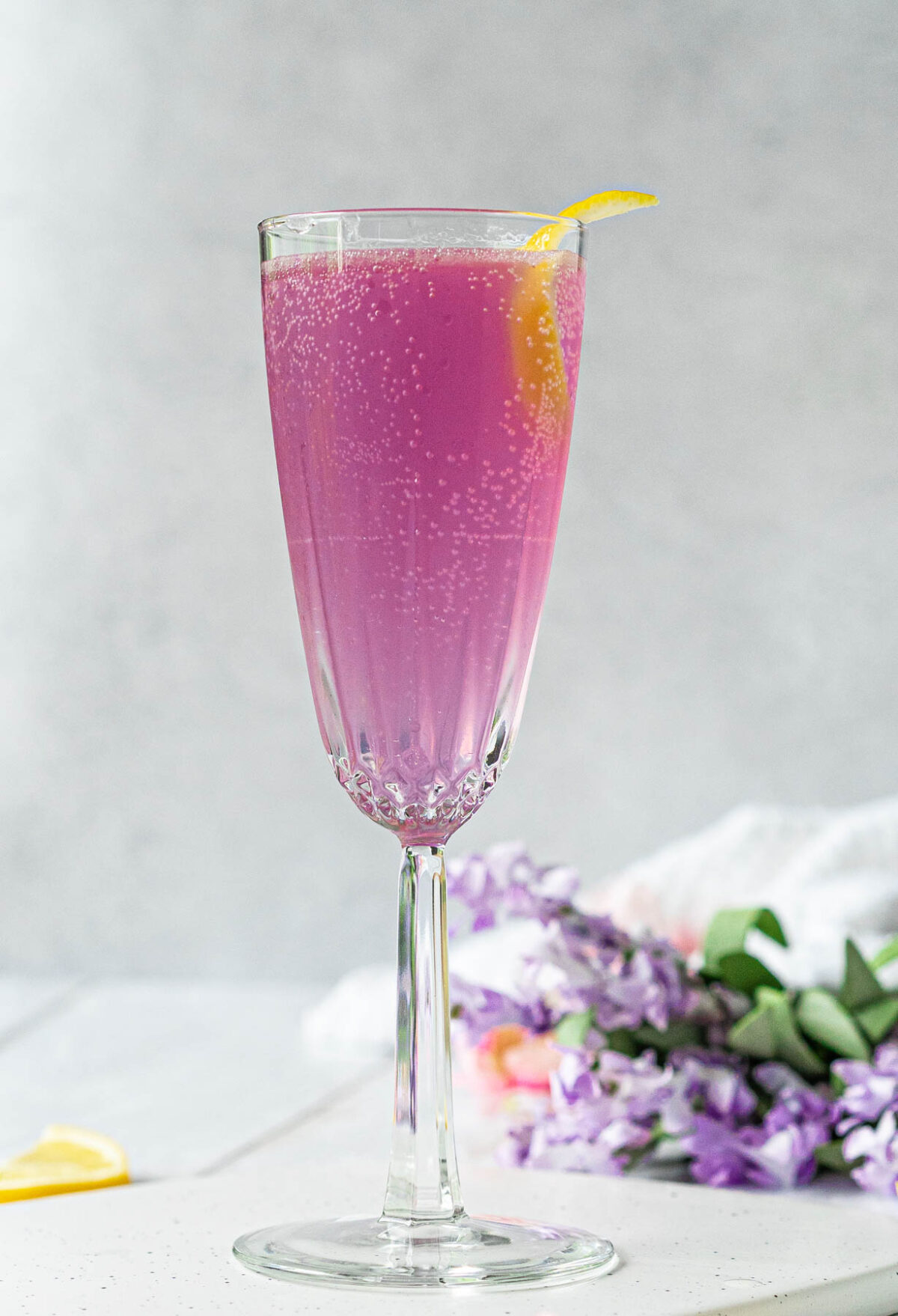 crystal champagne flute filled with a pale purple bubbling cocktail and garnished with a lemon twist