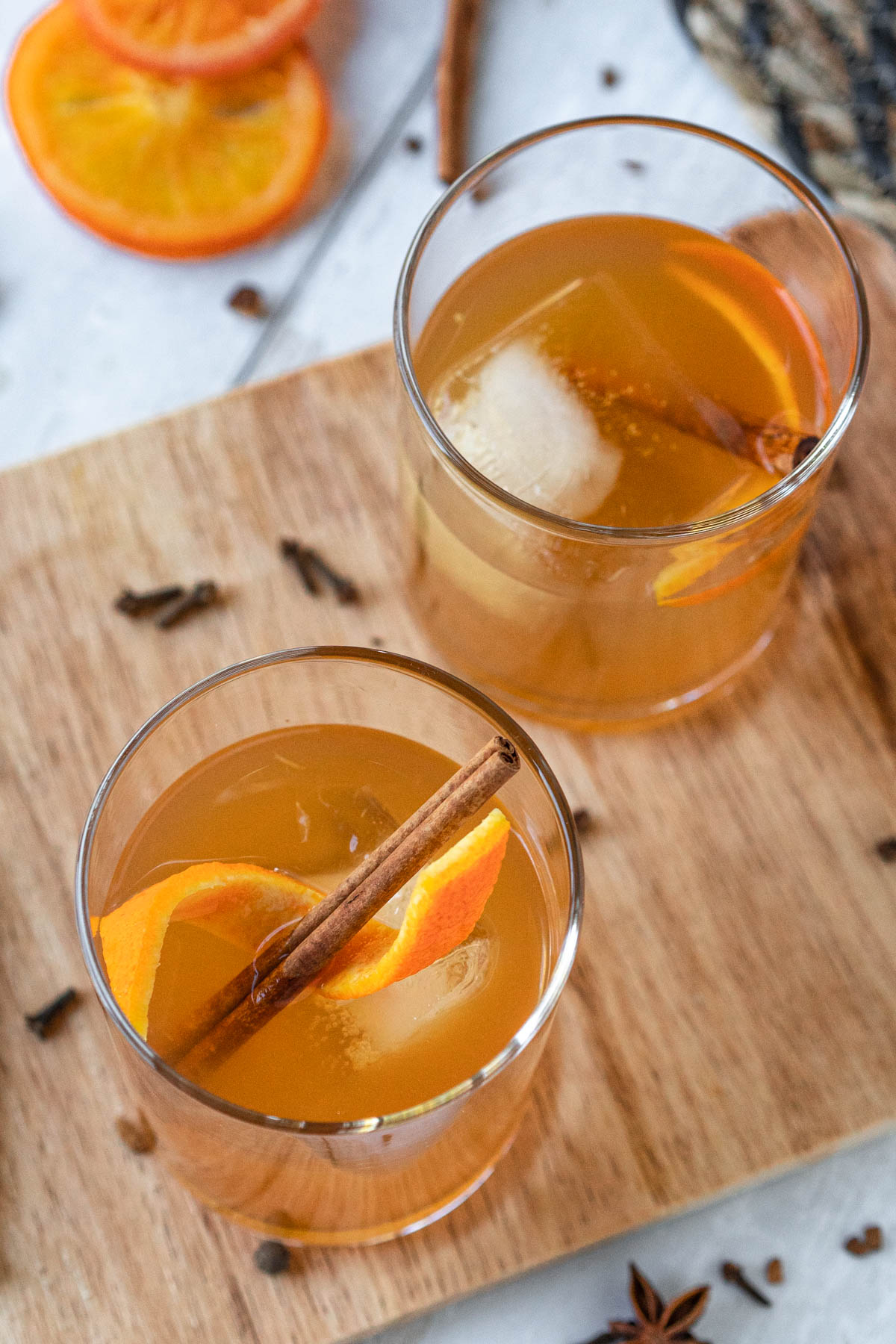 top-down view of two rocks glasses filled with an apple cider cocktail and an ice cube and garnished with an orange twist and cinnamon stick