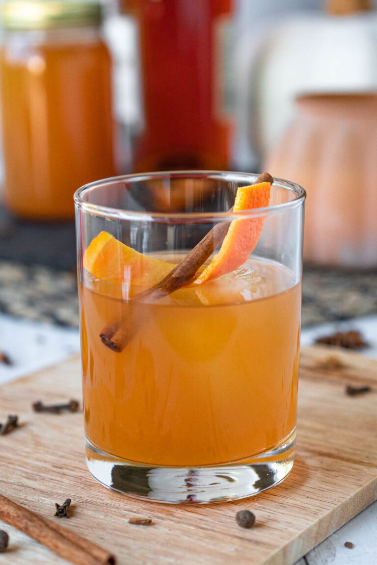 side view of a rocks glass filled with apple cider cocktail and garnished with an orange twist and cinnamon stick