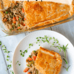 Top-down view of a rectangular slice of turkey pot pie on a small white plate, garnished with fresh thyme and rosemary. Above the plate is a baking dish of turkey pot pie with a slice missing. Text overlay at the top of the image reads, 'leftover turkey pot pie'