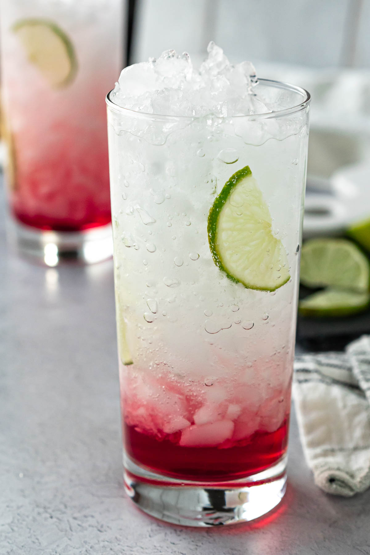closeup shot of two collins glasses filled with crushed ice, water, juice, and lime slices
