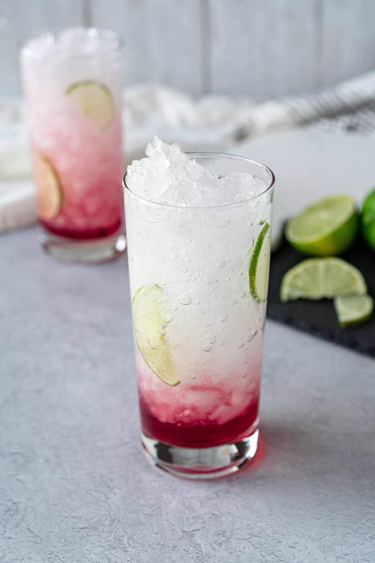 two collins glasses filled with crushed ice, water, juice, and lime slices