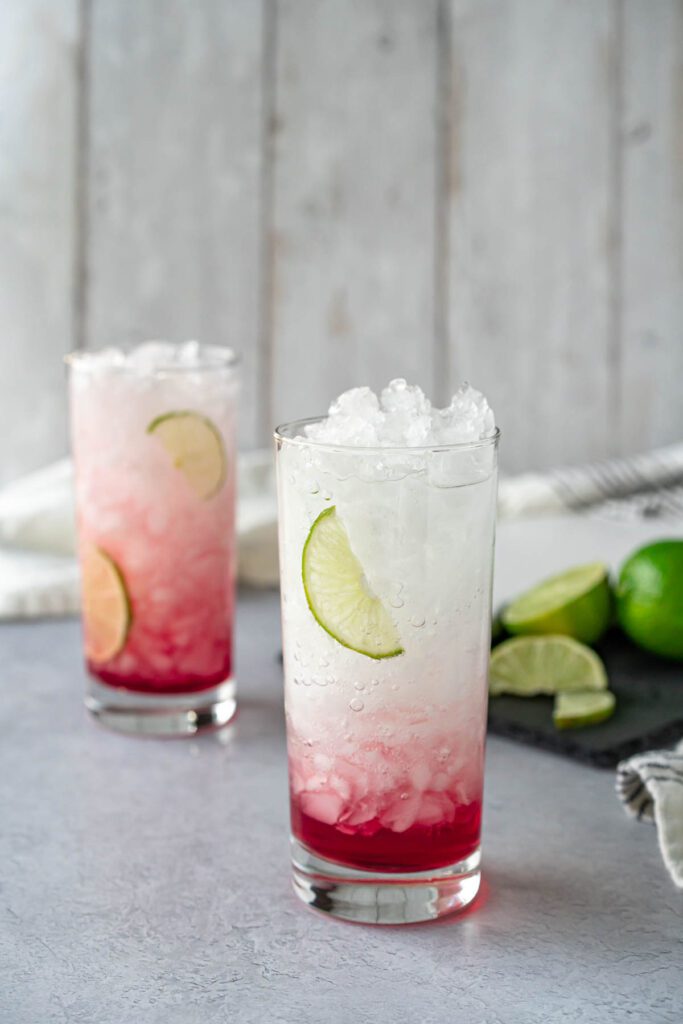 two collins glasses filled with crushed ice, water, juice, and lime slices
