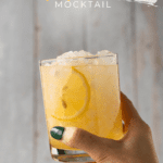 hand holding a rocks glass filled with crushed ice and a pale yellow drink with sliced lemon wedge garnishes