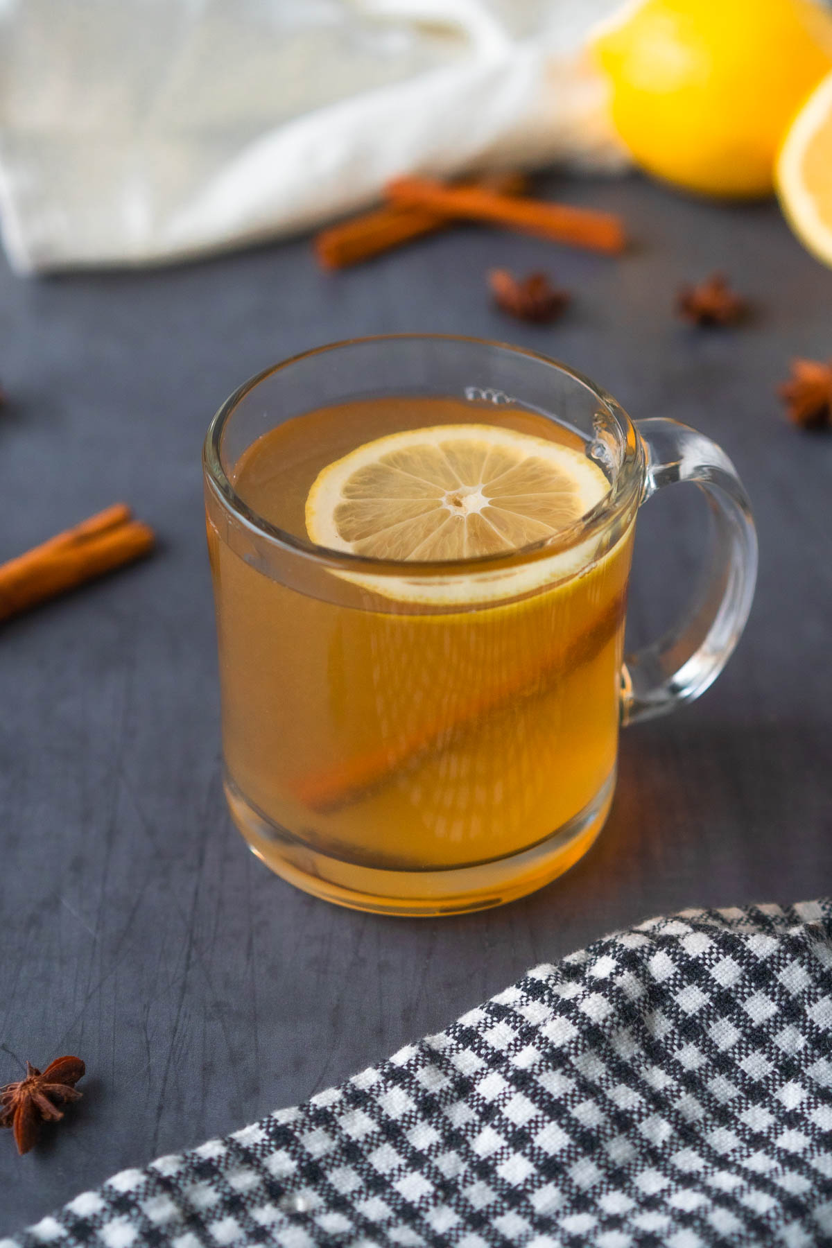 clear mug filled with an amber liquid and topped with a lemon slice and cinnamon stick