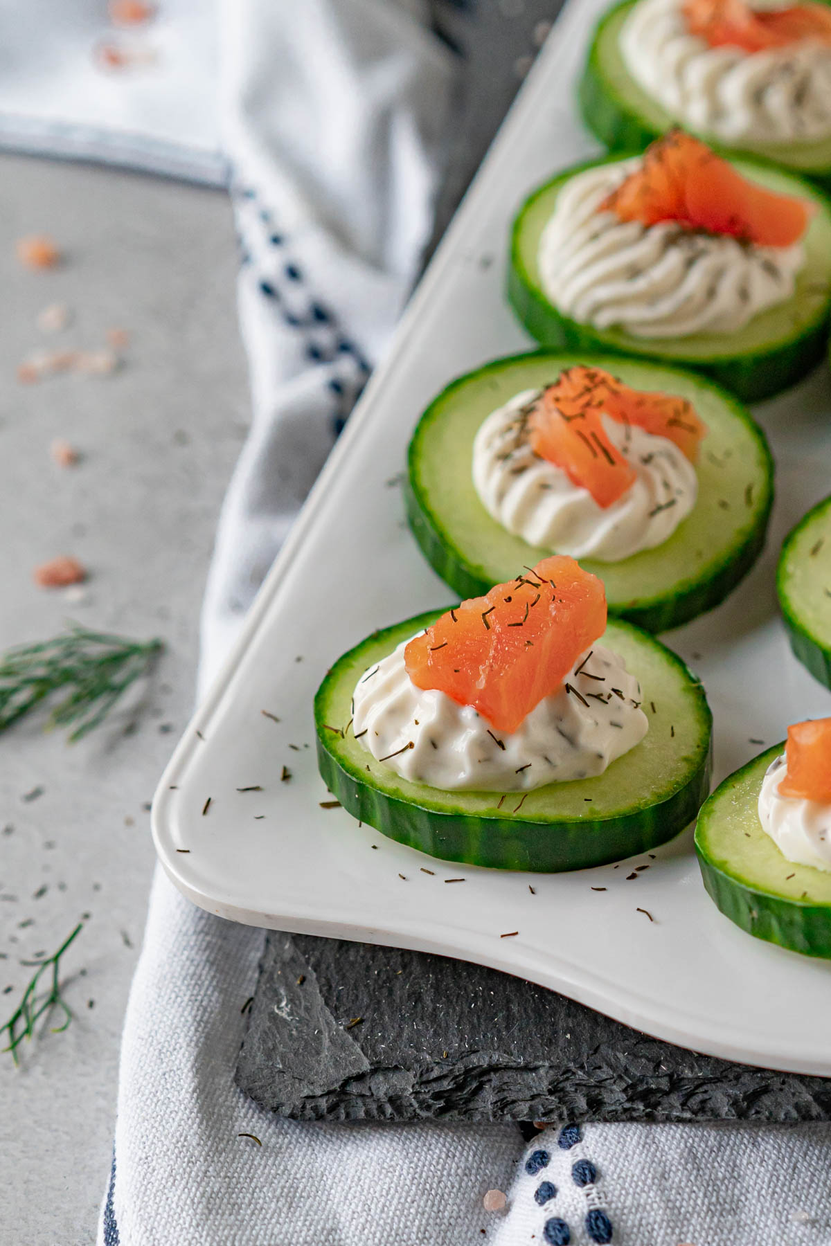 closeup shot of sliced cucumbers on a tray topped with cream cheese and smoked salmon