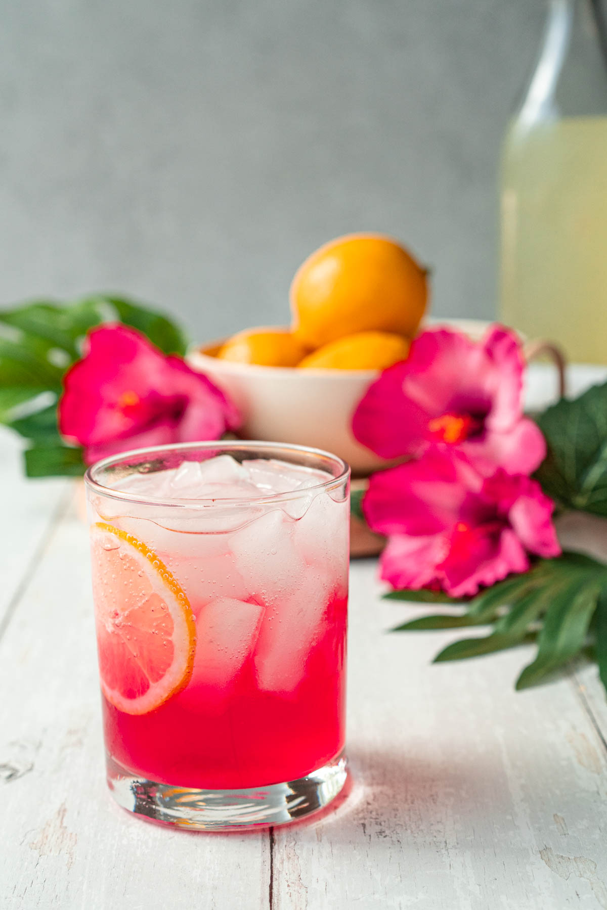a hot pink bubbly drink with ice and lemon slices