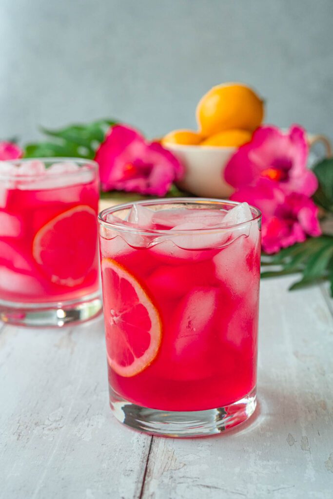 Two short glasses of a hot pink drink with ice and lemon slices